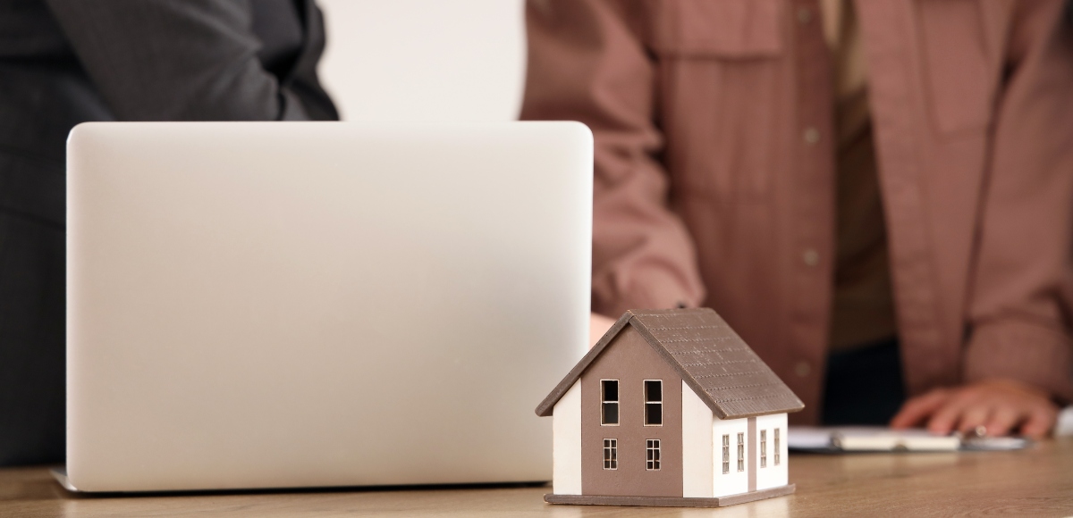 Dos personas consultando un laptop y una casita decorativa encima de la mesa
