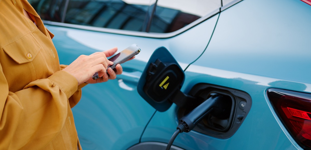 Mujer mirando el móvil mientras carga el coche eléctrico