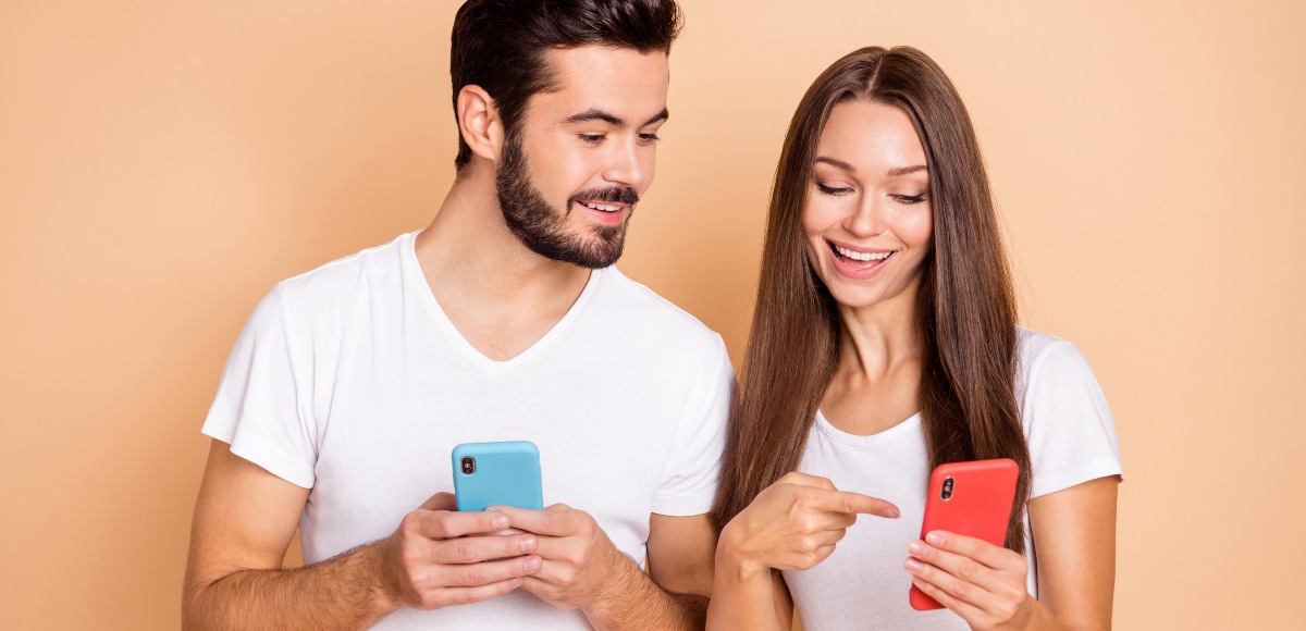 Un jove i una noia somrients mirant el telefono movil