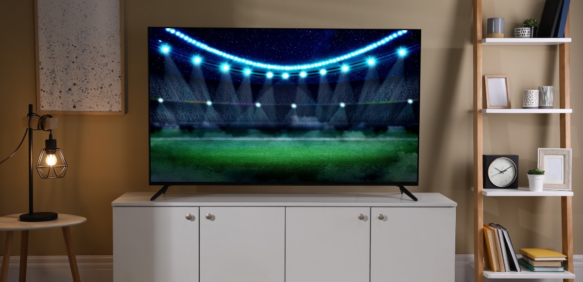 Salón con televisor encendido y partido de fútbol en la pantalla