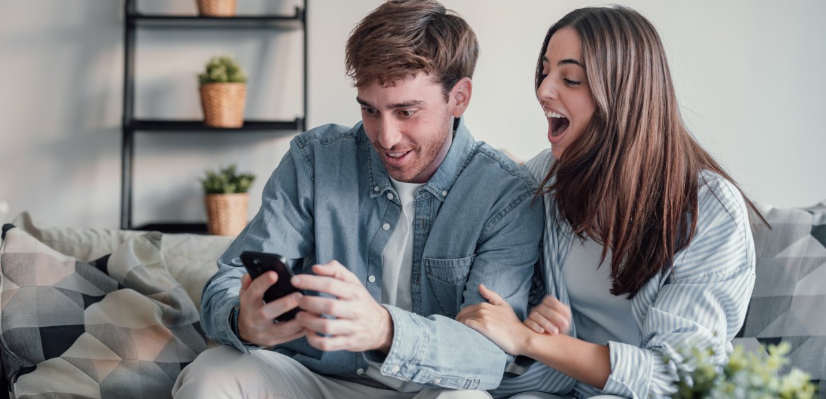 Pareja sonriente mirando el teléfono móvil sentados en el sofá de casa